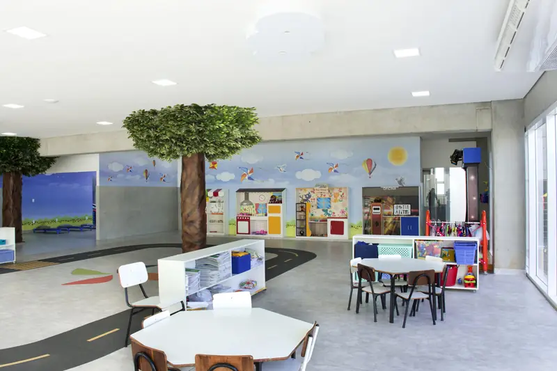 Espaço da Educação Infantil com árvore cenográfica, mesas baixas e pista desenhada no chão