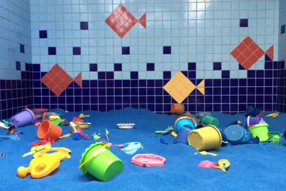 Área de brincar com brinquedos de praia e parede de azulejos com peixes