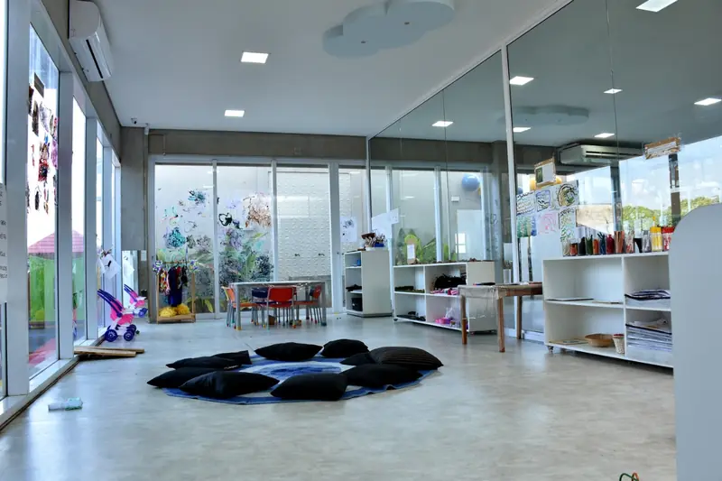 Sala ampla e iluminada com almofadas no chão e estantes de materiais