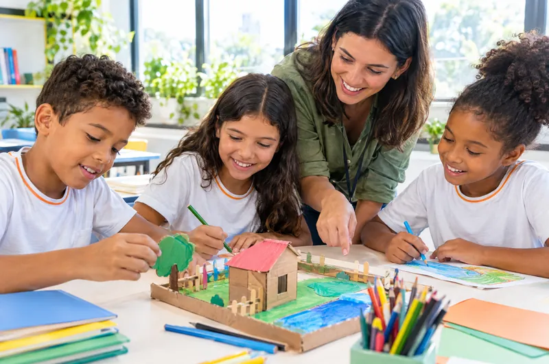 Alunos do Fundamental I montam uma maquete de papelão com a professora, numa sala iluminada