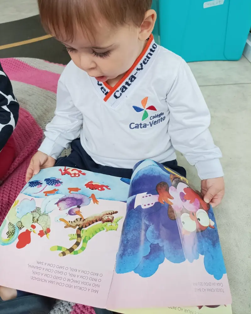 Criança de uniforme do Cata-Vento folheando um livro ilustrado